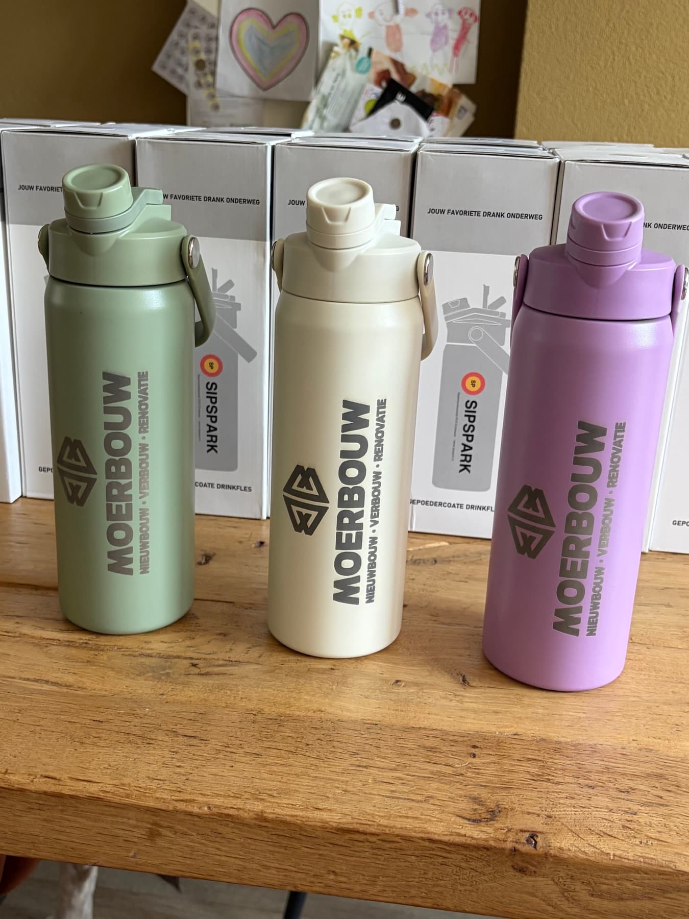 Drie gepersonaliseerde SipSpark-flessen in saliegroen, crème en lavendel met het logo van Moerbouw